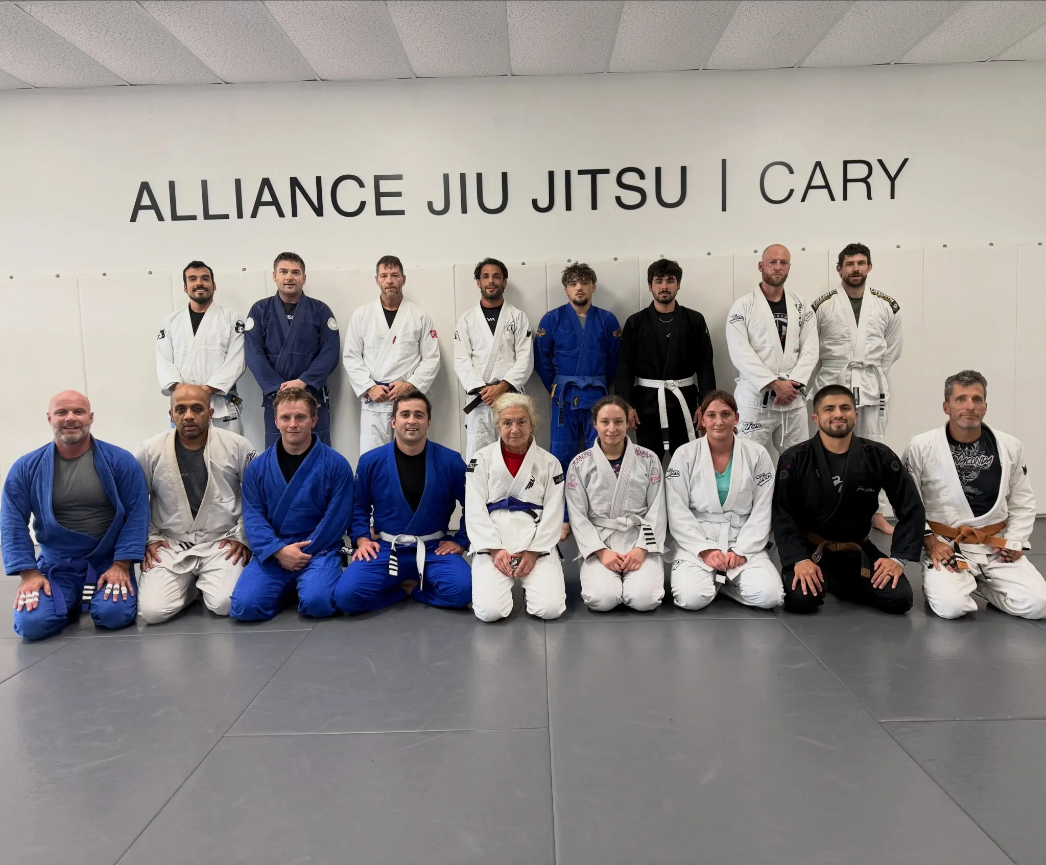 Adult Team Casarez students in gis lined up beneath the Alliance Jiu Jitsu Cary wall sign